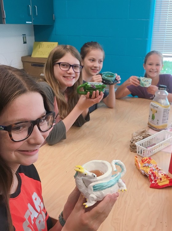Sixth graders in the art room show off mugs that they made.