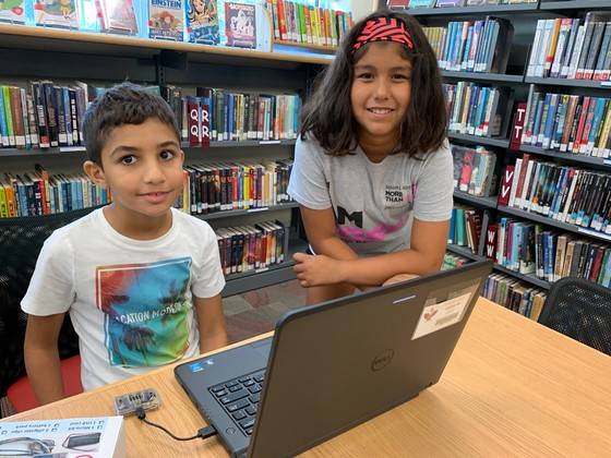 Two students, a boy and a girl smile while working on a laptop in Clermont Elementary's library.