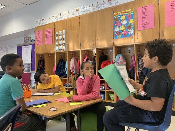 Photo of three students sitting at a table, sharing their work