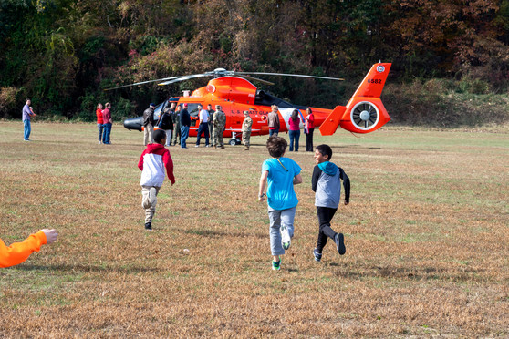 Students on the upper field run towards an orange helicopter.