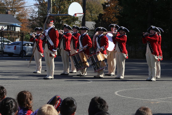A fife and drum team perform for Clermont students on the blacktop.