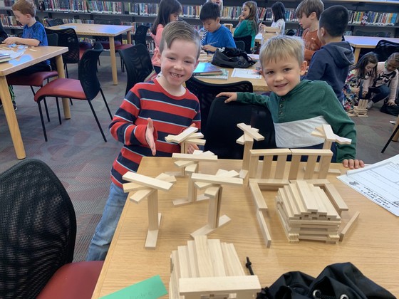 Students in the library build structures with wooden blocks and planks.