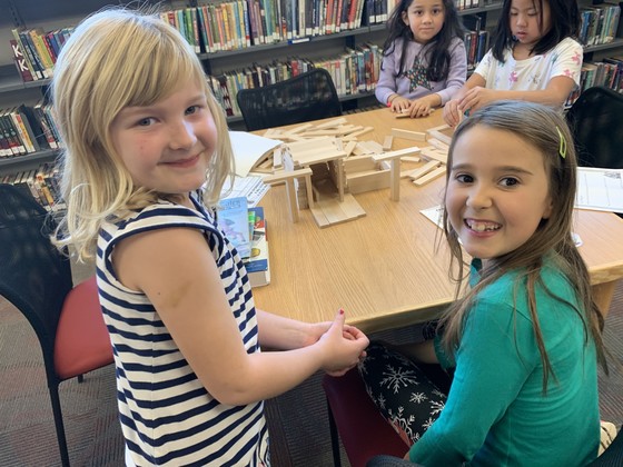 Students in the library build structures with wooden blocks and planks.