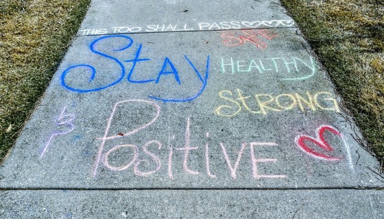 Sidewalk chalk on a driveway saying "Stay positive, healthy, strong. This too shall pass."