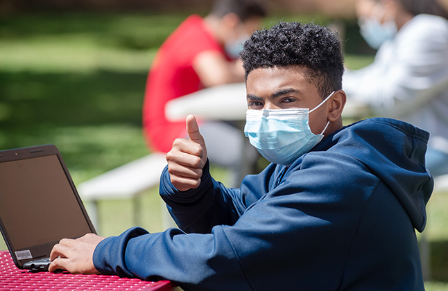 photo of male student in a mask giving a thumbs up outside