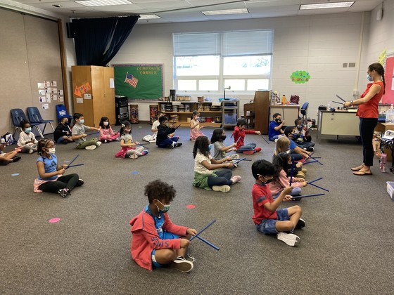Photo of children in music class sitting on the floor and playing rhythm sticks