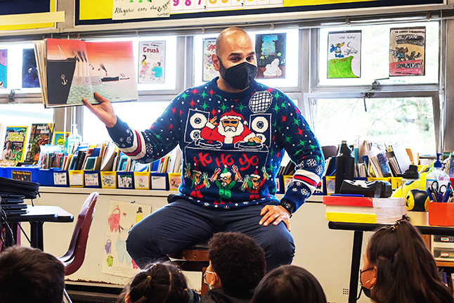 photo of Daryl Yarmolvich reading to students dressed in a holiday sweater