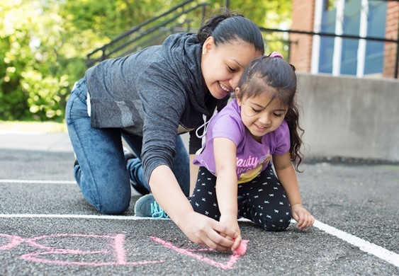 Photo of child and mother drawing with sidewalk chalk