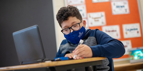 Elementary student using a pen and wearing a face mask. 