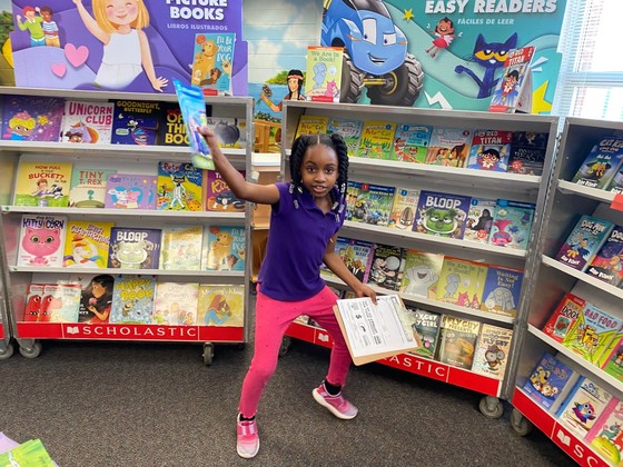Photo of a student holding up a book at the book fair preview day in the library