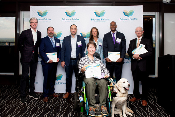 Group photo of six people standing plus one woman in a wheelchair with a service dog. 