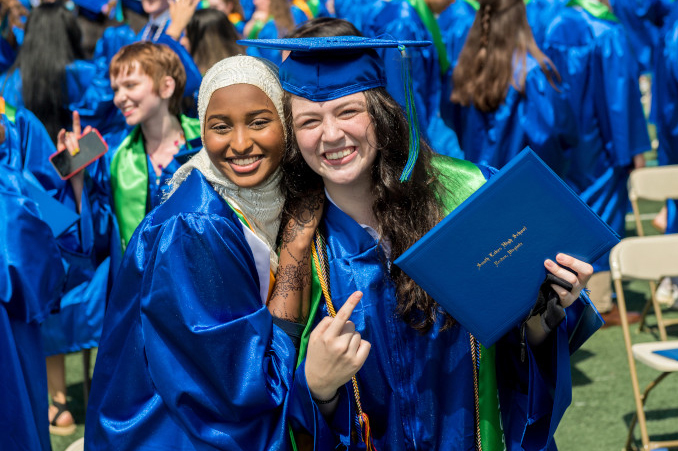 Two students in graduation gowns, one holding a diploma