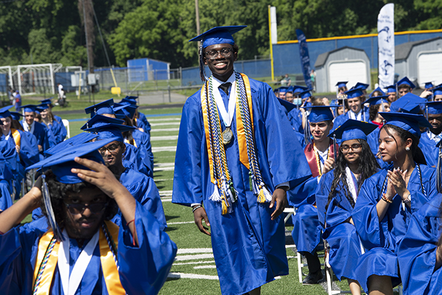 Smiling student in cap and gown walks down an aisle at a graduation ceremony