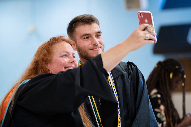 Teacher takes a selfie with a student in graduation gown