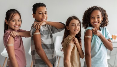Four smiling students show off bandaids on their right upper arms. 