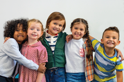 Five young children of diverse backgrounds with their arms around each other smiling for a camera. 