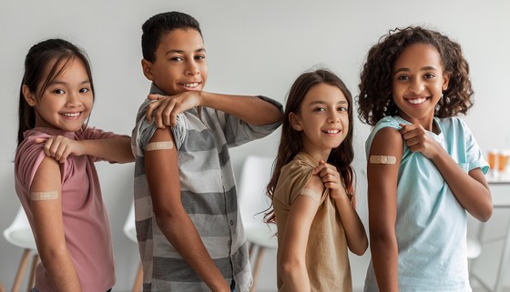 Four children show off bandaids on their upper arms. 