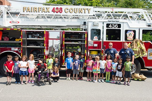 A large group of young students outside, standing in front of a fire truck
