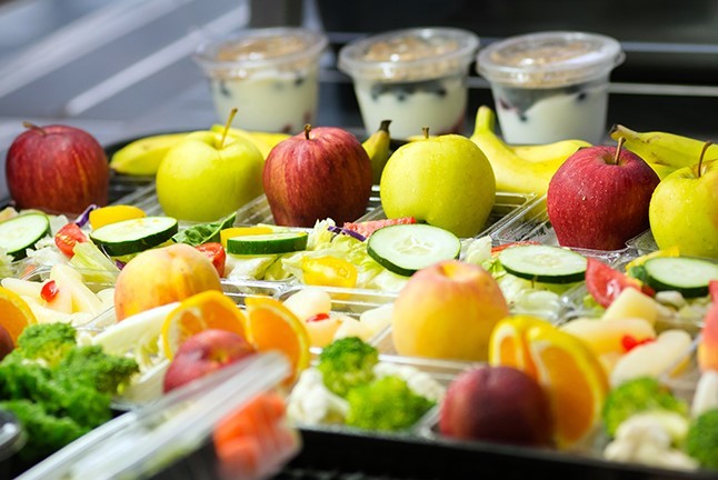several salads and pieces of fruit in a lunch line