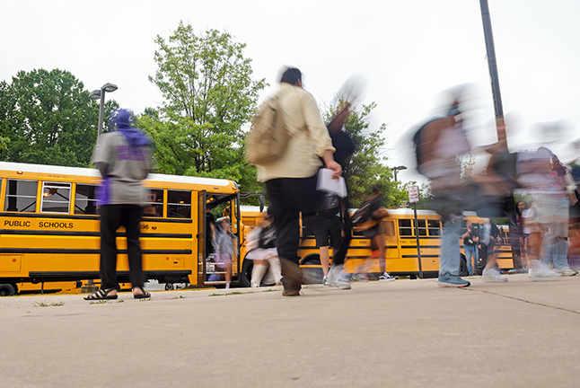 A rush of children come off school buses. 