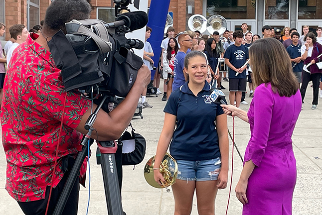 A Woodson student holds a brass instrument while being interviewed for the news. 