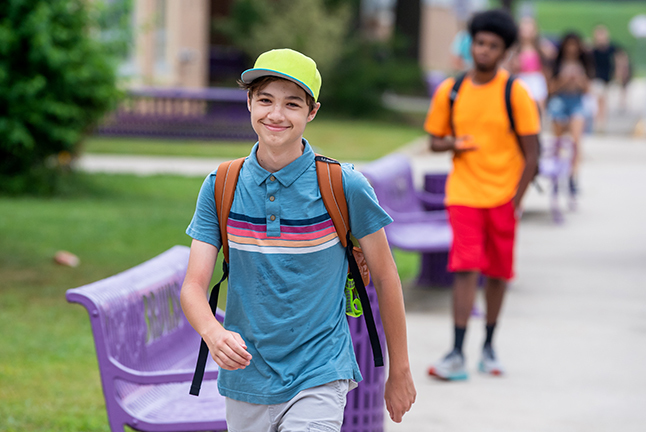 A middle school male student walks to school while smiling