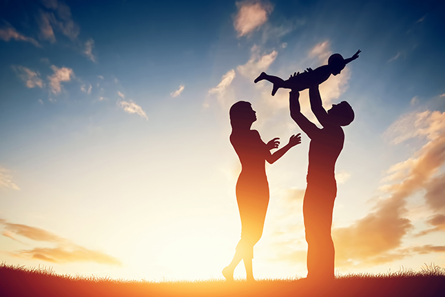 A silhouette of a man and woman holding up a child against a sunset. 