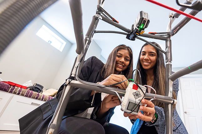 Two students photographed through the bars of a walker they modified to help people with Parkinsons