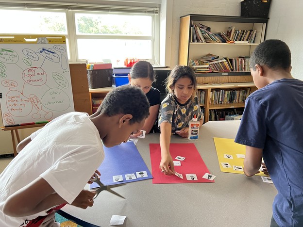 Four students lean over a table to sort pictures into four categories.