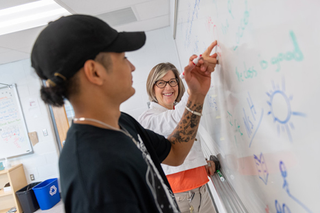 A teacher looks on as a student works on a white board