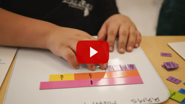 Student's hands, working with math manipulatives, with a youtube playback button overlayed. 