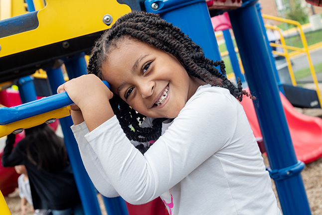 A girl smiles on a piece of playground equipment