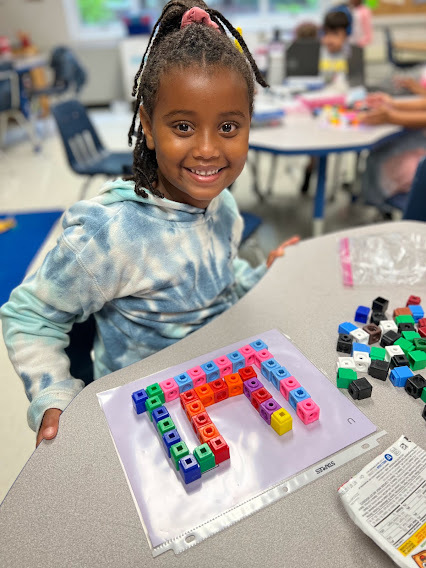 A first grade student sits at her table with colorful blocks organized on her table