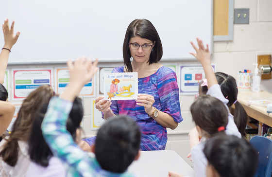 A teacher reads to students who have their hands up