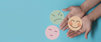 hands hold a paper happy face. worried and angry  faces lay nearby