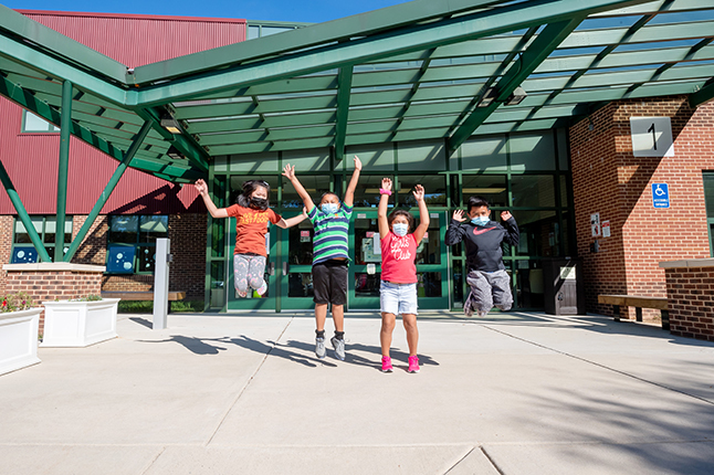 Four students jump outside of a school building. 