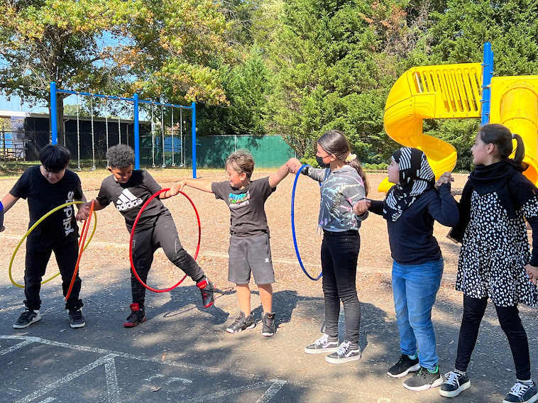 A line of fourth grade students passes a hula hoop along the row while holding hands