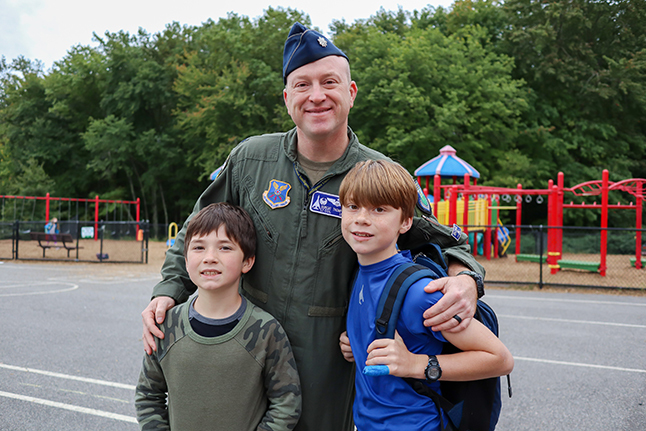 A father in military uniform stands with two sons. 