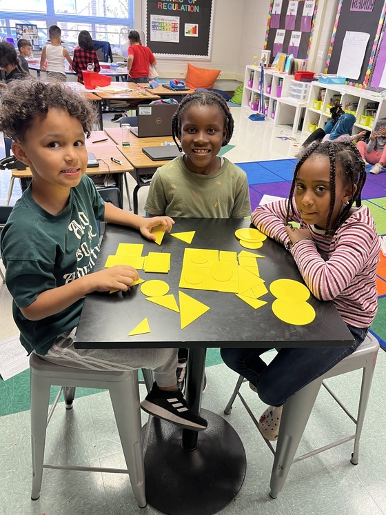 Three students sitting at a small table with yellow shapes on it