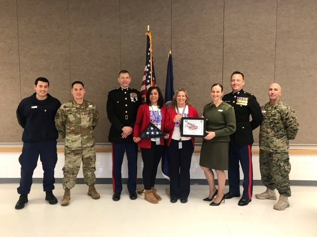An image of Armed Forces members presenting a flag of the United States to Principal Salata and Assistant Principal Younger.