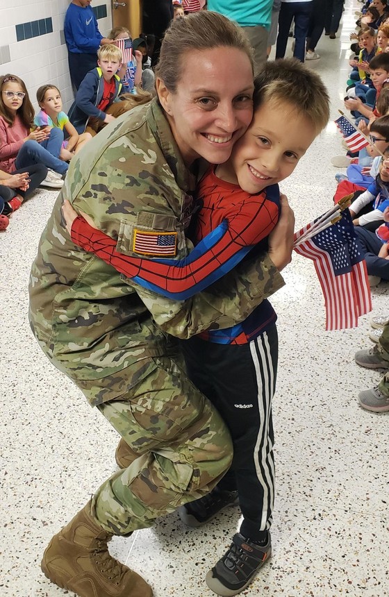 A mother in military uniform hugs her child at Clermont's Veterans Day event.