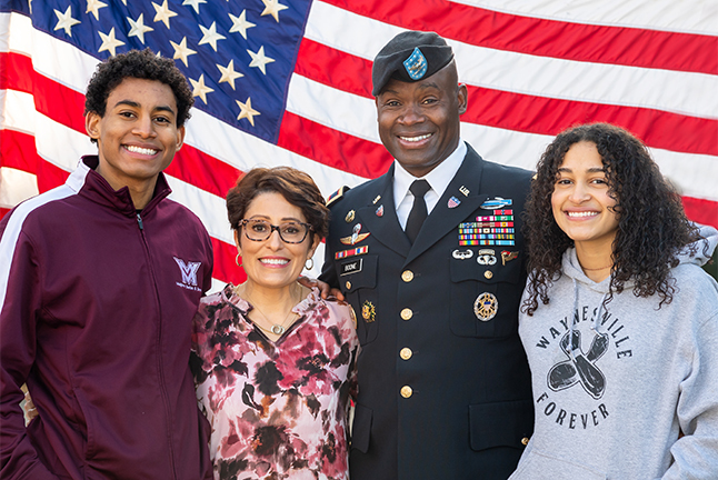 A military family smiles for a portrait in front of a flag