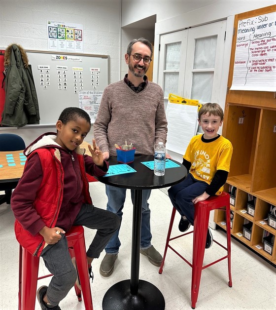 Two students and an adult smiling in a classroom while they are participating in a math activity