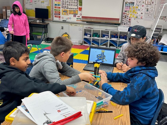 Four students sit at a table and work on a LEGO project together