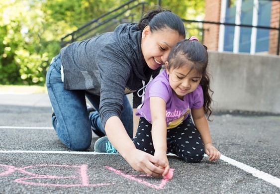 Mother and child write in  chalk on a playground