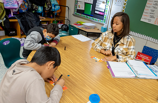 A teacher watches two students work