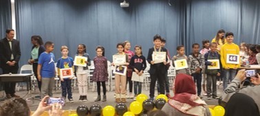 Students who participated in the spelling bee stand on stage