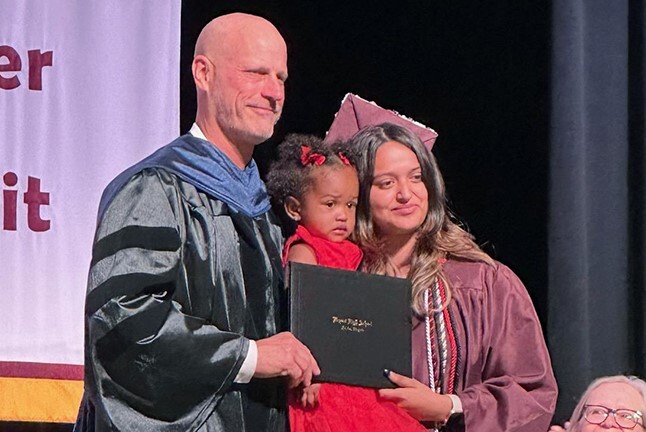 2023 Graduate Anyeli Salguero holding her daughter while receiving diploma