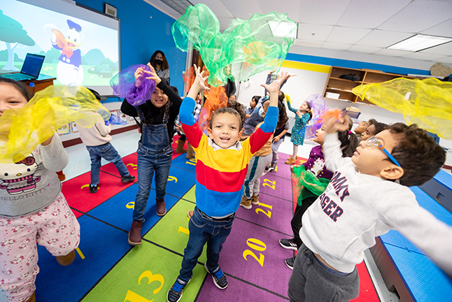 Elementary students in a very colorful classroom setting tossing colorful "fluffs" above them. 
