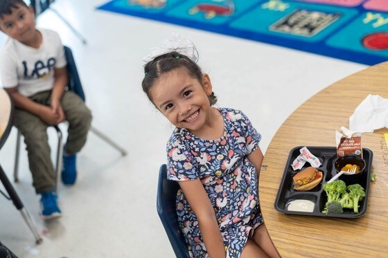 Child sitting in cafeteria with school lunch on table
